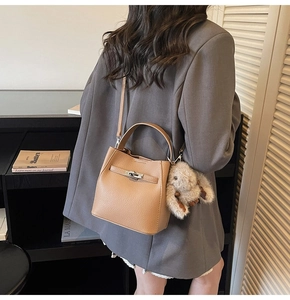 Close-up of brown lychee grain leather bucket bag with metal turn-lock and rabbit charm