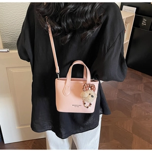 Detail of pink lychee leather crossbody bucket bag with plush puppy charm on side