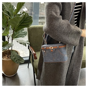 Detail of denim crossbody box bag with brown leather trim and metal chain strap