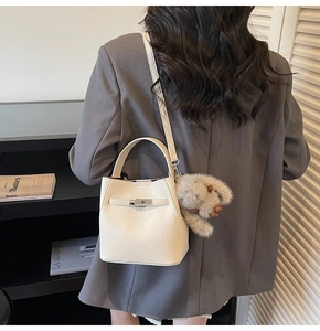 Detail of off-white lychee grain bucket bag with metal turn-lock and plush puppy charm