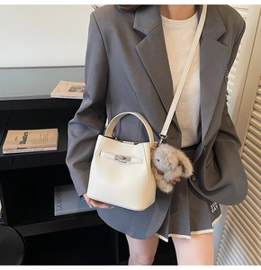 Chic beige bucket bag with metal lock and plush rabbit charm shown on a stylish model