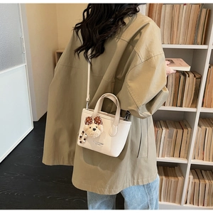 Detailed view of cream leather bucket bag with cute bear charm on a khaki trench coat