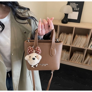 Detail of a brown lychee-textured mini bucket bag with a plush teddy bear charm