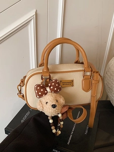 Chic beige bowling bag with brown handles and a cute plush teddy charm on a black book