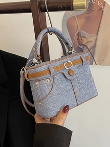 Denim box handbag with decorative belt and jean pocket details on a wooden hanger