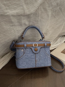 Retro denim handbag with brown leather trim and metal rivets in a stylish studio setting
