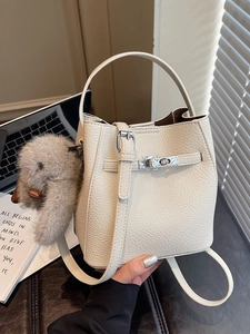 Chic beige bucket bag in lychee leather with metal lock and plush charm on desk