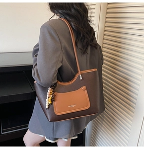 Close-up of stylish two-tone faux leather tote bag with beaded charm and shoulder strap