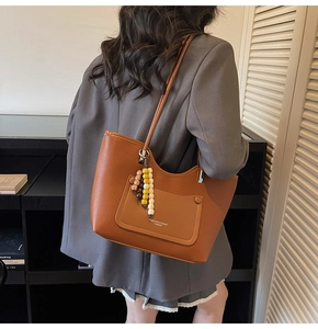 Detail of brown lychee grain leather tote bag with colorful beaded charm and brand logo