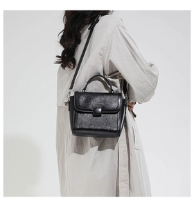 Detail of a black square crossbody bag with glitter textured flap and top handle