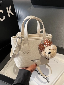 White lychee leather bucket bag with top handles, crossbody strap, and plush bear charm