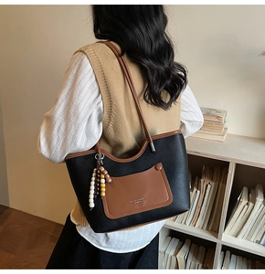 Detail of a large leather tote bag featuring black litchi grain and brown contrast pockets