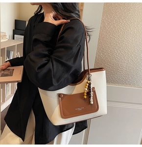 Close-up of white lychee leather tote bag with brown pocket and wooden bead charm