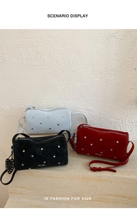 Three studded crossbody bags in blue, black, and red displayed on stone steps