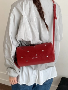 Red leather barrel crossbody bag with silver star studs worn by a model in casual attire
