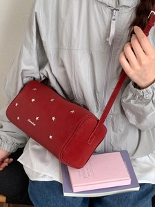 Red cylindrical faux leather shoulder bag with silver star rivets shown on a model