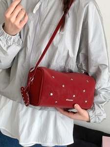 Deep red cylinder crossbody bag featuring silver star rivets and a heart charm detail