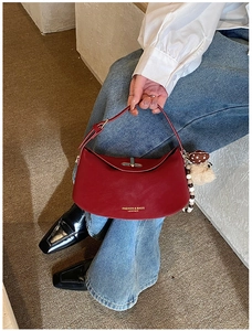 Détail du sac polochon en cuir rouge avec breloque ours porté par un mannequin de mode