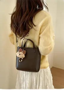Sac seau en cuir marron avec breloque ours, porté par un mannequin en style minimaliste