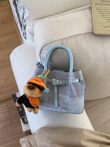 Light blue textured bucket bag with puppy charm on a soft cream sofa setting