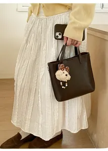 Détail d'un sac seau en cuir marron foncé avec un charmant ours en peluche sur un mannequin