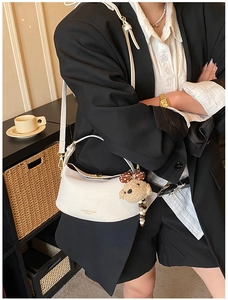 White faux leather crescent bag with plush bear charm worn with a modern blazer