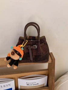 Vintage brown patterned hobo bucket bag with a cute puppy pendant on a bookshelf