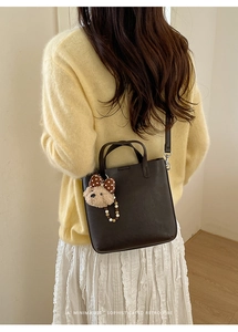 Détail du sac seau en cuir marron foncé avec breloque ours et bandoulière amovible