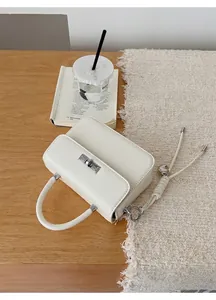 Detail der cremeweißen Lederhandtasche mit silbernem Drehverschluss und Herzanhänger auf Holztisch