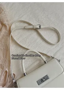 Detail einer cremefarbenen Handtasche mit Silber-Drehverschluss und schmalem Schultergurt