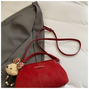 Red crossbody bag with plush bear charm and fashion label on a minimalist background