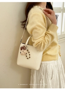 Détail du sac seau crème minimaliste avec breloque ours et nœud à pois décoratif