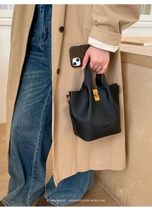 Détail du sac seau noir grainé avec boucles dorées porté sur un trench-coat beige