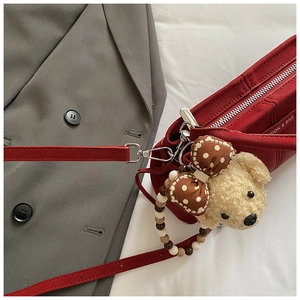 Close-up of red crossbody bag with cute teddy bear charm on grey blazer background