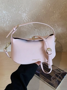 Sac à main en cuir rose avec détails dorés et bandoulière sur une table en bois