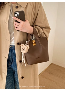 Detail of dark brown leather bucket bag with gold twist lock and cute plush bear charm