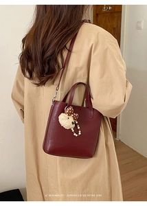 Détail du sac seau bordeaux avec breloque ours porté sur un trench-coat kaki