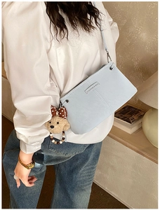 Detail of light blue crossbody bag with plush bear charm and metallic brand tag
