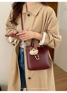 Détail du sac à main en cuir bordeaux porté avec un manteau et un charm ourson