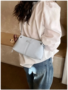 Detail of light blue crossbody bag with bear charm and silver fashion logo on model