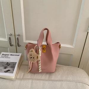 Sac seau rose en cuir grainé avec breloque d'ours sur un canapé au ton chaud
