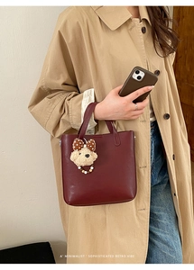 Détail du sac cabas bordeaux en cuir avec breloque ours à nœud pour un style rétro chic