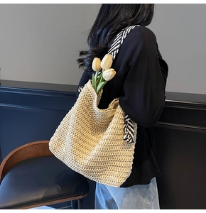 Detailed hollow-out woven texture of beige straw tote bag with striped shoulder strap