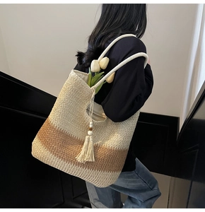 Detail of woven gradient straw tote bag featuring tassel charm and long shoulder straps