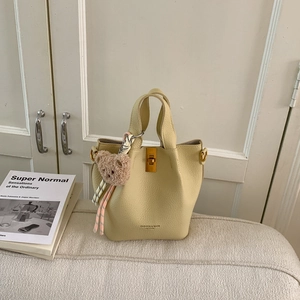 Détail du sac seau beige avec texture litchi, fermoir en métal et breloque petit ours