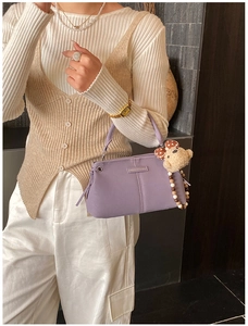 Detail of lavender PU leather crossbody bag featuring a metal logo plate and teddy bear charm
