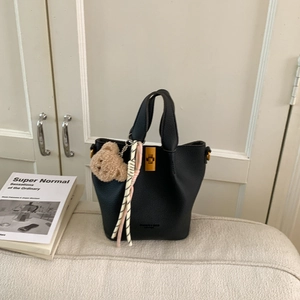 Détail du sac seau noir avec fermoir doré, peluche d'ours et foulard rayé décoratif