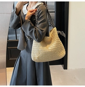 Detail of woven straw tote bag featuring black and white striped silk scarf shoulder strap