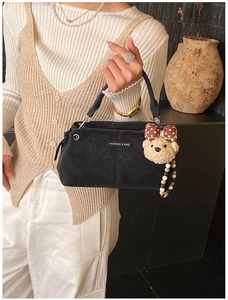 Detail of black crossbody bag with matte texture, fashion tag, and cute bear pendant charm