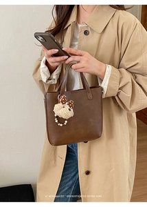 Détail d'un sac seau rétro marron foncé avec un porte-clé ours en peluche sur la bride